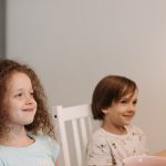 Two children sitting at a table smiling, enjoying their breakfast time indoors.