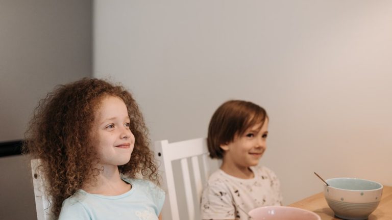 Two children sitting at a table smiling, enjoying their breakfast time indoors.